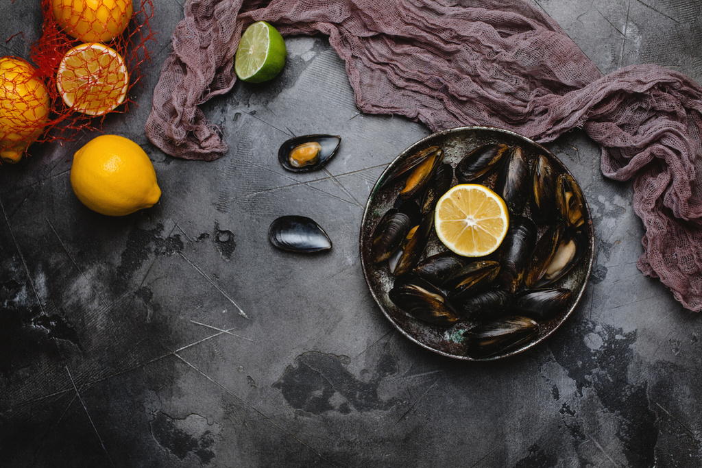 top view of gourmet mussels with shells on vintage plate and citrus fruits on grey   - Photo, Image