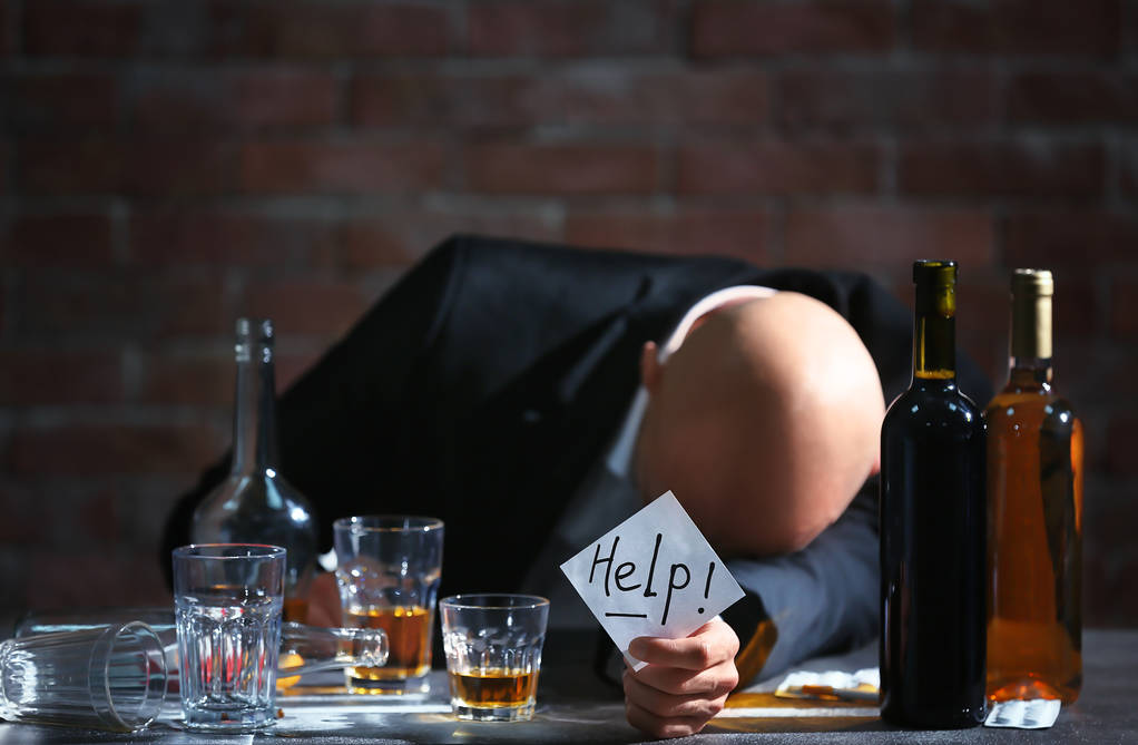 Homem bêbado sentado à mesa e segurando papel com a palavra AJUDA. Conceito de alcoolismo
 - Foto, Imagem