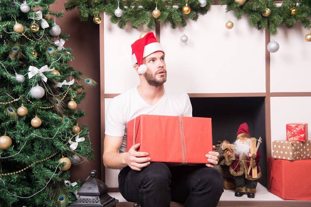 Kerl mit ernstem Gesicht im Weihnachtsmannhut hält Geschenkbox - Foto, Bild
