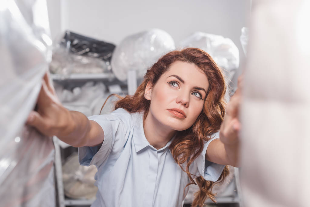 female dry cleaning worker looking at clothing packed in plastic bags - Photo, Image