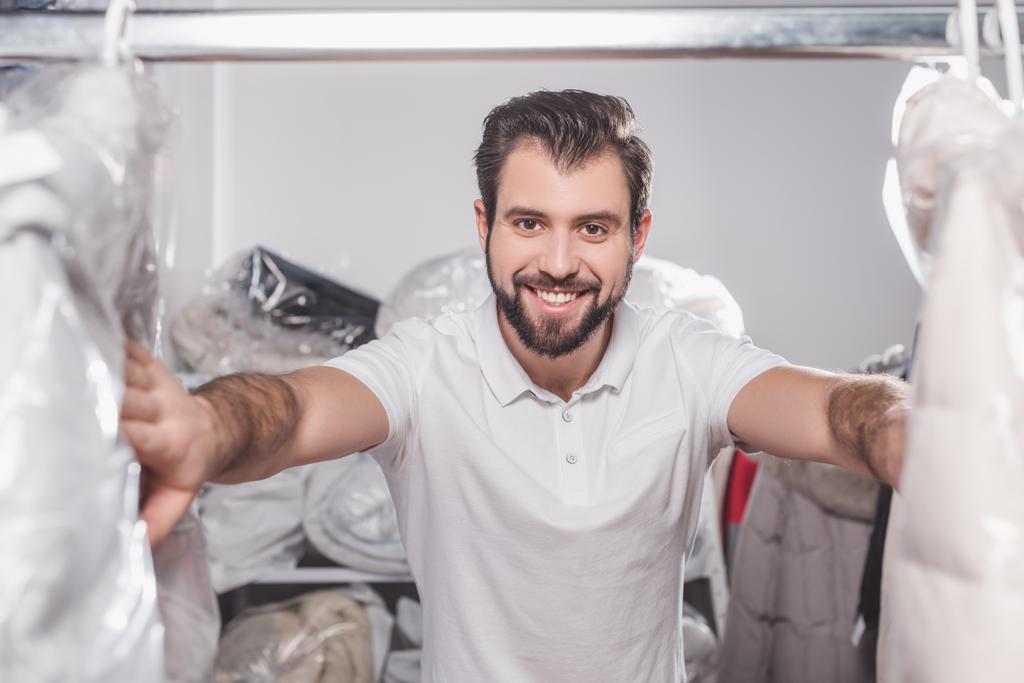 работник химчистки на складе с одеждой, упакованной в пластиковые пакеты
 - Фото, изображение