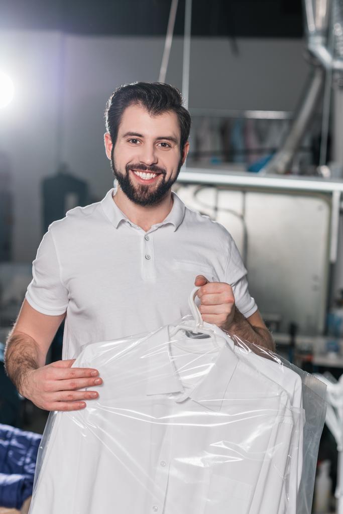 Trabajador de limpieza en seco con camisa limpia en percha en bolsa de plástico
 - Foto, imagen