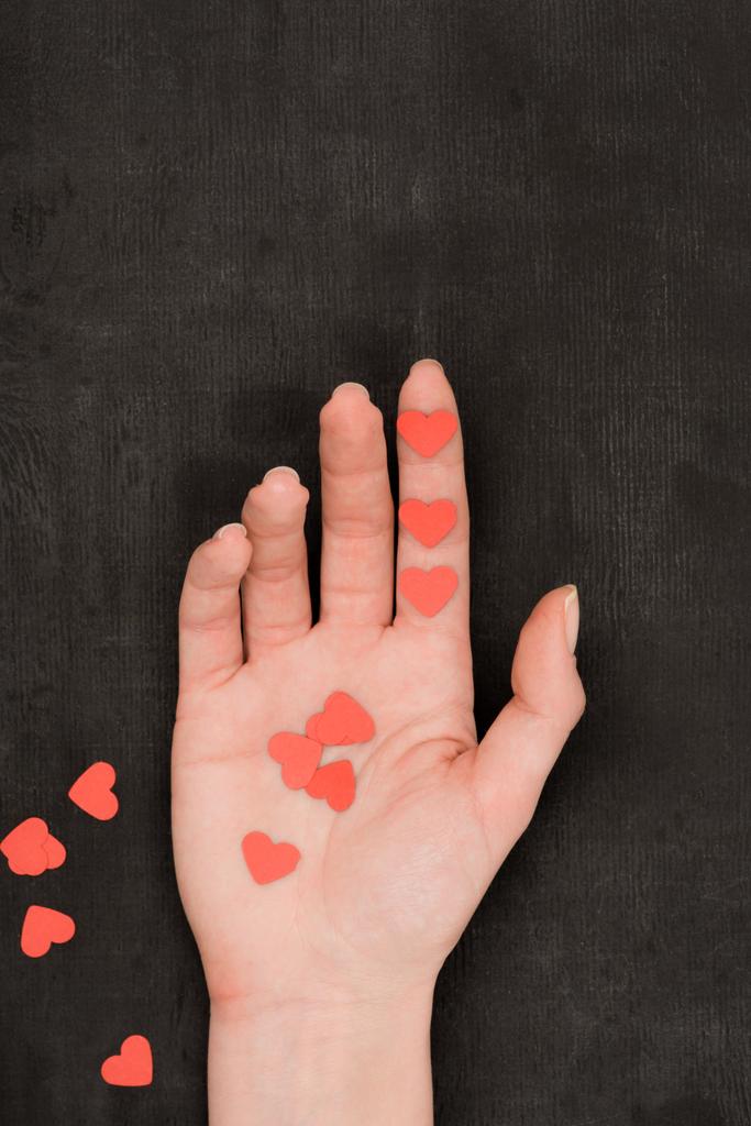 Teilansicht weiblicher Hand und rotem herzförmigem Konfetti auf dunklem Hintergrund, Valentinstag-Konzept - Foto, Bild