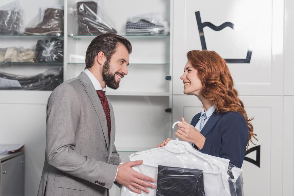 dry cleaning manageress giving bag with clothes to happy man - Photo, Image