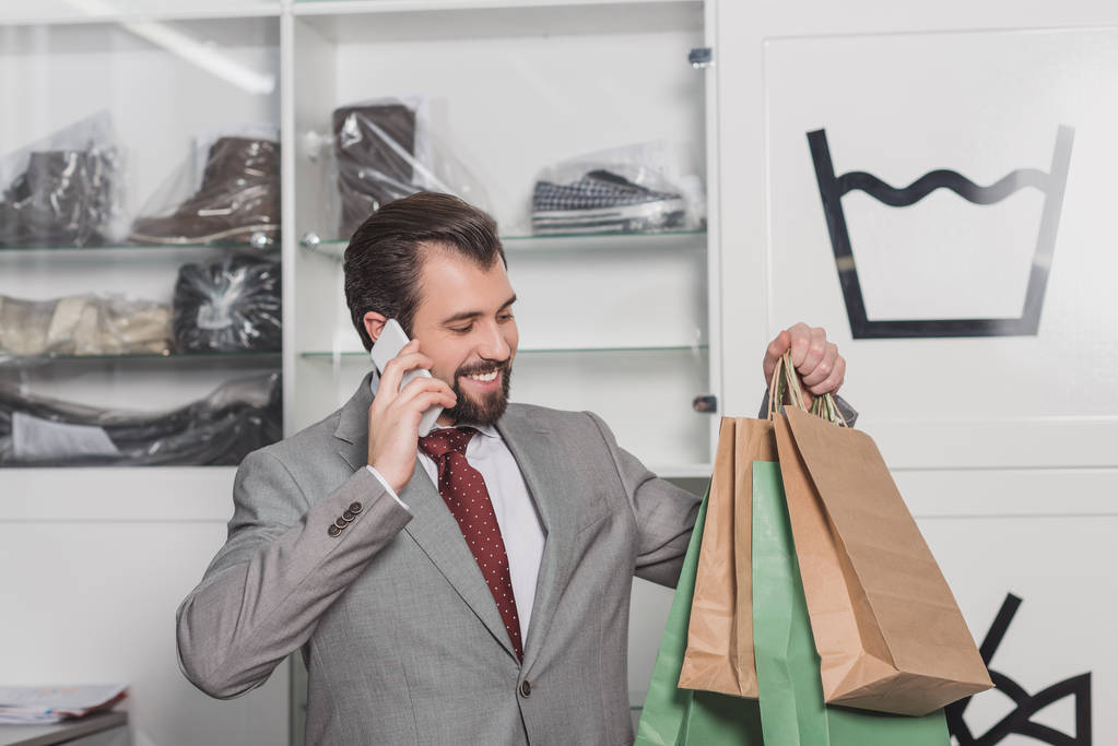 handsome young businessman with paper bags talking by phone - Photo, Image
