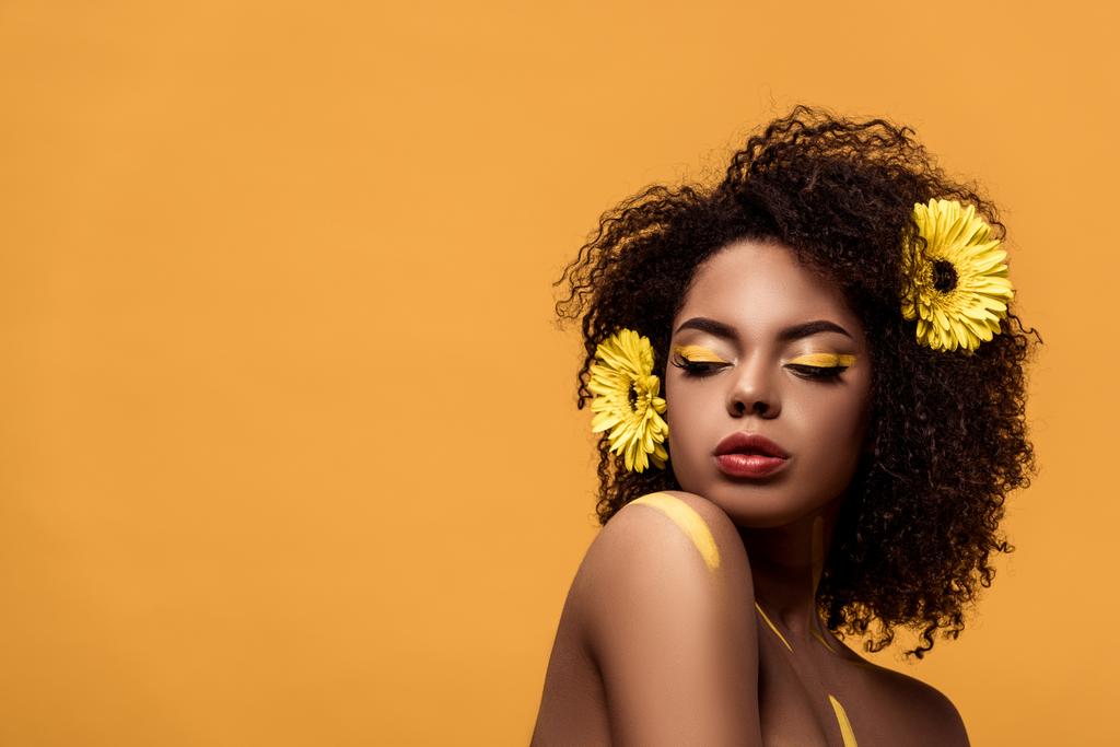 Şehvetli Afro-Amerikan olan kadın sanatsal makyaj ve saç üzerinde turuncu arka plan izole gerbera - Fotoğraf, Görsel