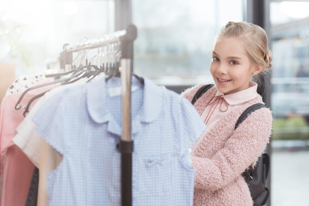 χαμογελαστό παιδί που επιλέγουν ρούχα σε κρεμάστρα στο κατάστημα  - Φωτογραφία, εικόνα