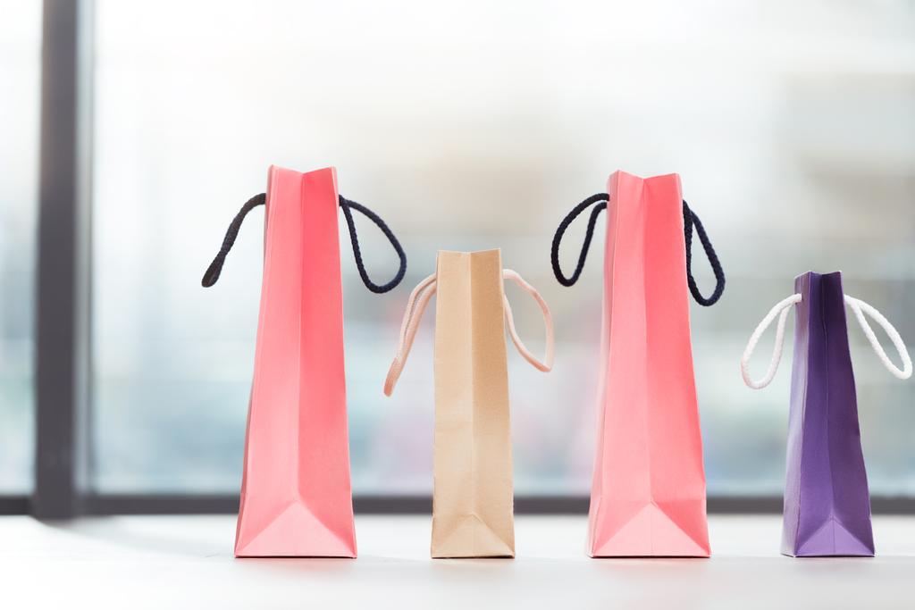 gekleurde papieren zakken te leggen in een rij op oppervlak tegen raam  - Foto, afbeelding
