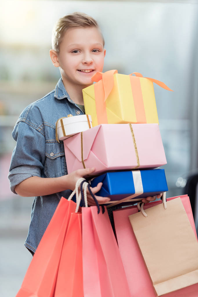 garçon souriant tenant des boîtes avec des sacs en papier dans les mains à l'intérieur du magasin
    - Photo, image