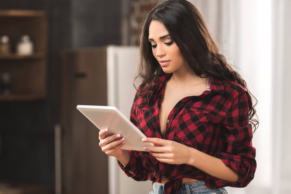 ελκυστικό κορίτσι στο καρώ πουκάμισο χρησιμοποιώντας ψηφιακό tablet στο σπίτι - Φωτογραφία, εικόνα