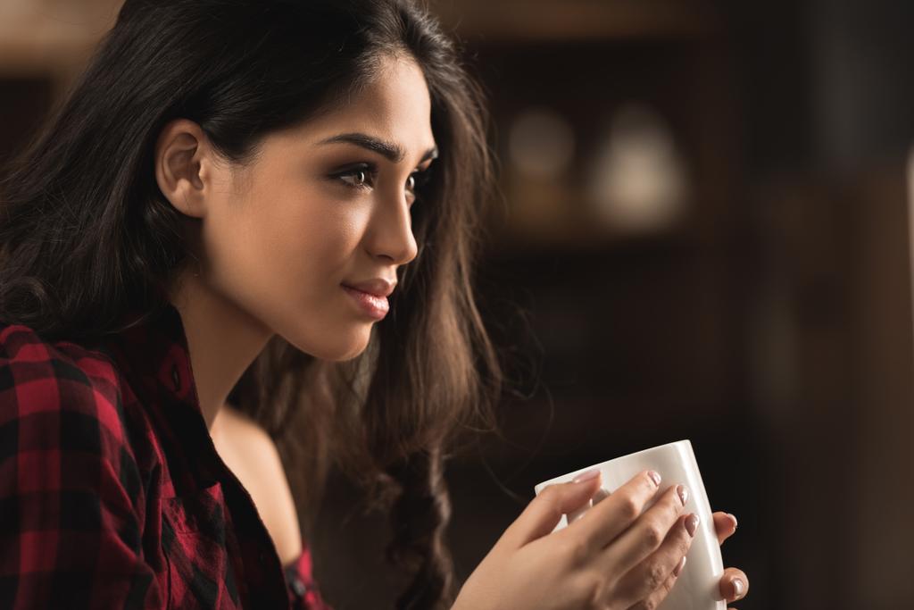 boční pohled na krásné mladé ženy držící šálek kávy a hledat dál - Fotografie, Obrázek