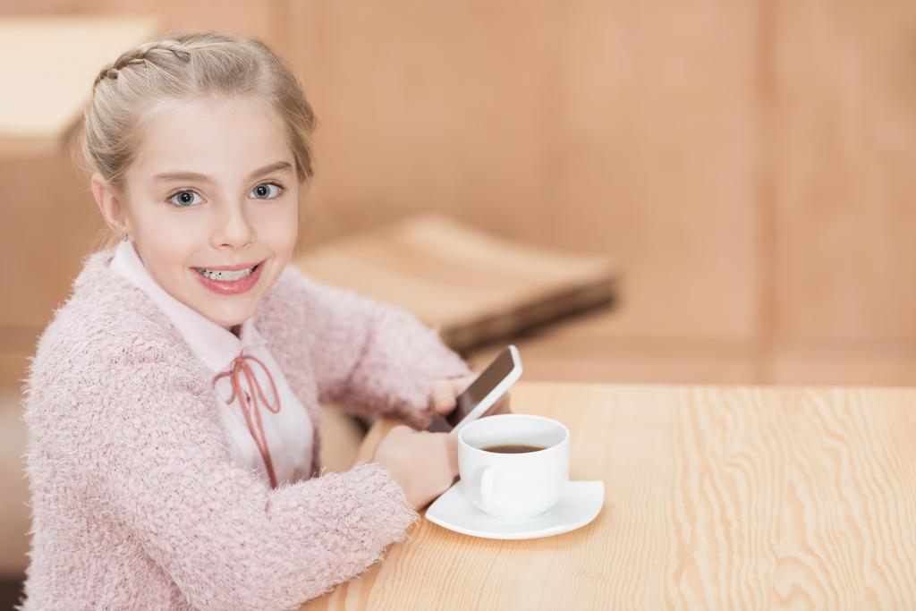enfant souriant assis à table avec smartphone dans les mains
  - Photo, image