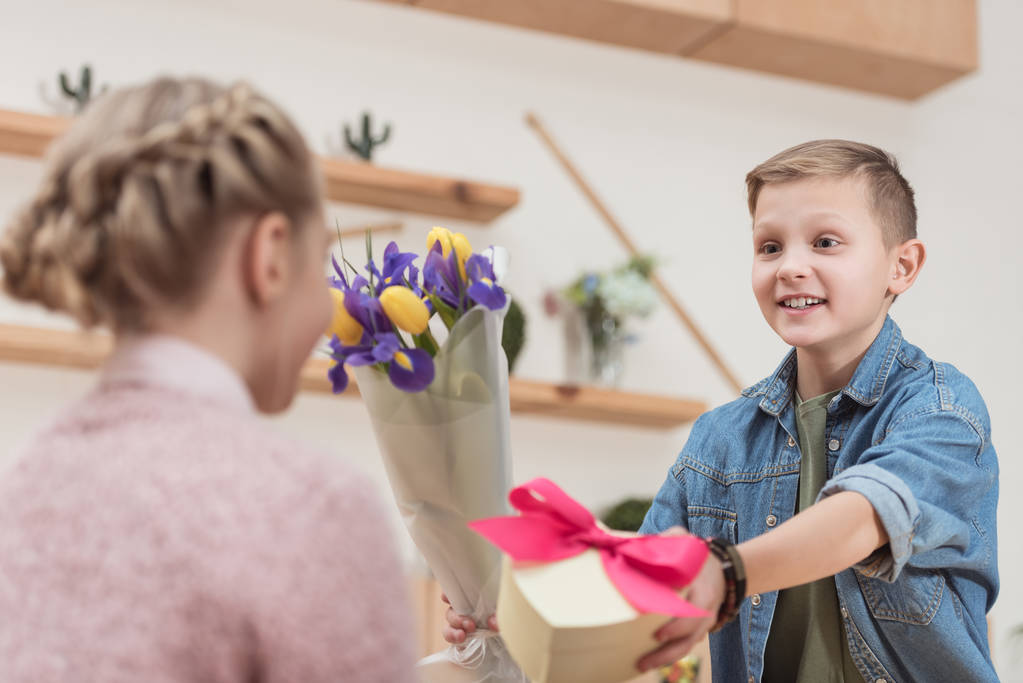 smiling boy presenting bouquet and box with ribbon to girlfriend at cafe   - Photo, Image