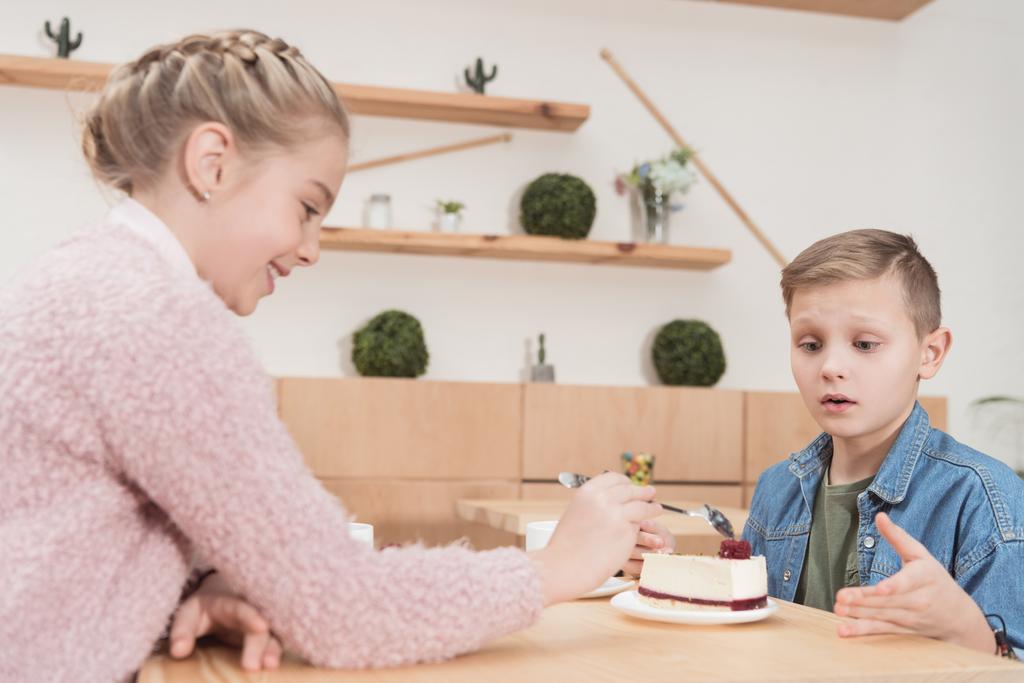 děti, které sedí u stolu v kavárně při pohledu na dort na stůl v kavárně  - Fotografie, Obrázek