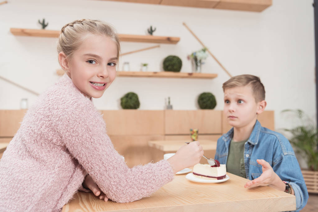 улыбающийся ребенок смотрит в камеру, сидя за столом напротив мальчика на другой стороне в кафе
  - Фото, изображение