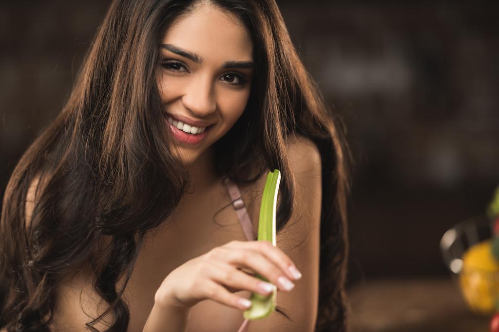 ελκυστική νεαρή γυναίκα τρώει σέλινο και να χαμογελά στη φωτογραφική μηχανή  - Φωτογραφία, εικόνα