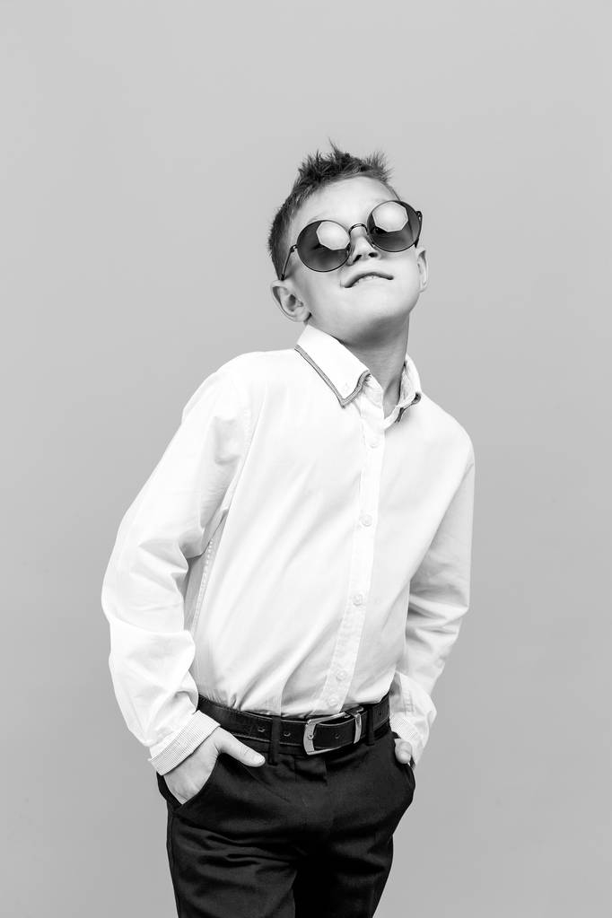 Criança elegante em camisa branca e calças pretas usando óculos de sol posando em estúdio
 - Foto, Imagem