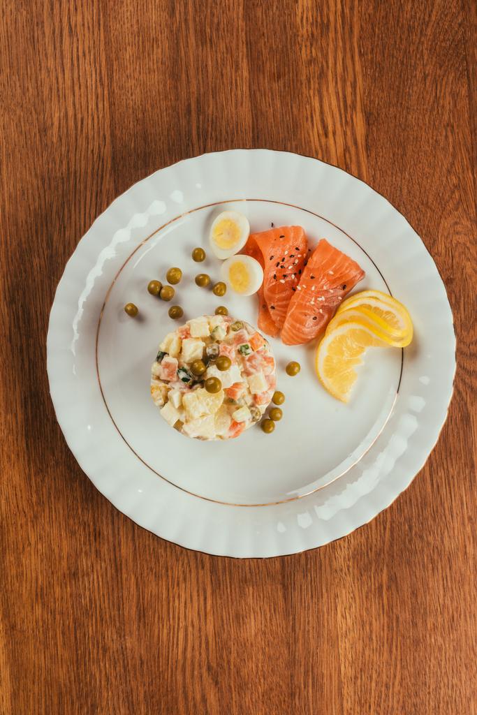 Russische salade op plaat met verspreide erwten, gekookte eieren en vis segmenten    - Foto, afbeelding