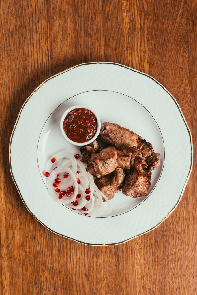 Το Top view στη σχάρα κρέατος με κρεμμύδι και σως ροδιού σπόρους στο άσπρο πιάτο στο ξύλινο τραπέζι - Φωτογραφία, εικόνα