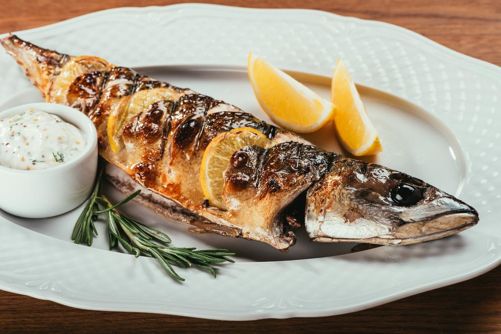 fried fish laying on white plate with orange slices and sauce over wooden surface   - Photo, Image