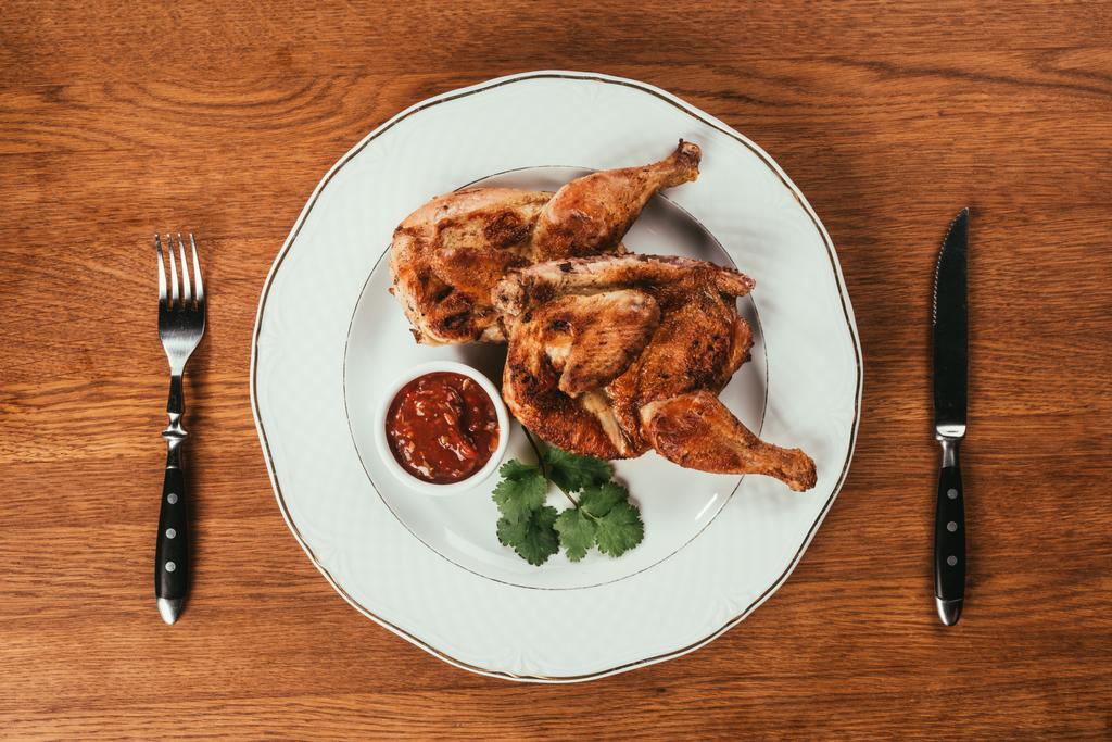 Bovenaanzicht van gegrilde kip geserveerd op plaat met saus op houten tafel - Foto, afbeelding