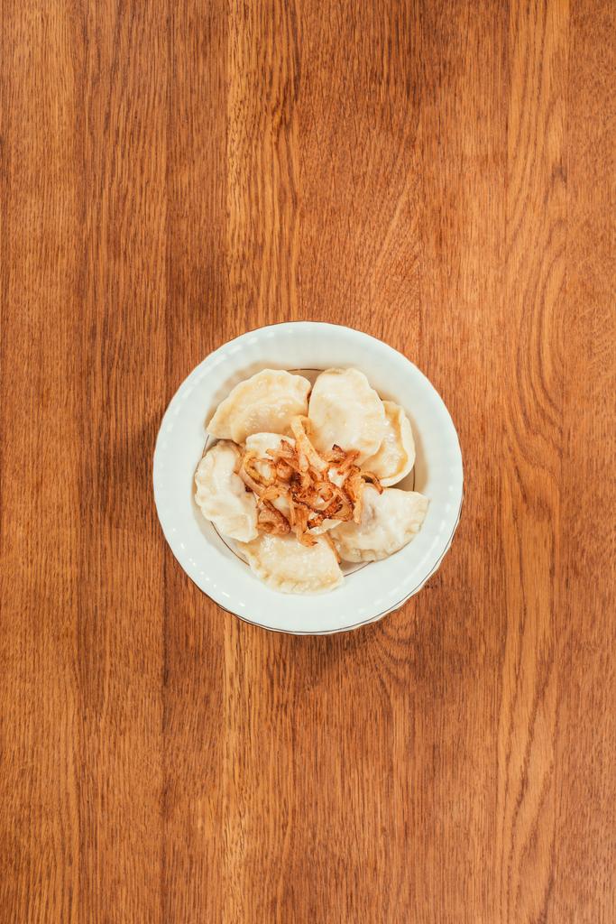 Knödel mit gebratenen Zwiebeln auf Teller über Holzoberfläche legen  - Foto, Bild
