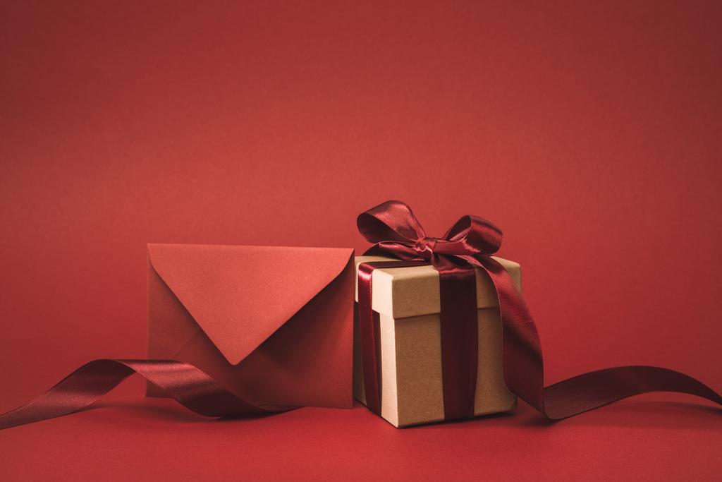 Nahaufnahme von leeren Umschlag und Geschenk mit Band isoliert auf rot - Foto, Bild
