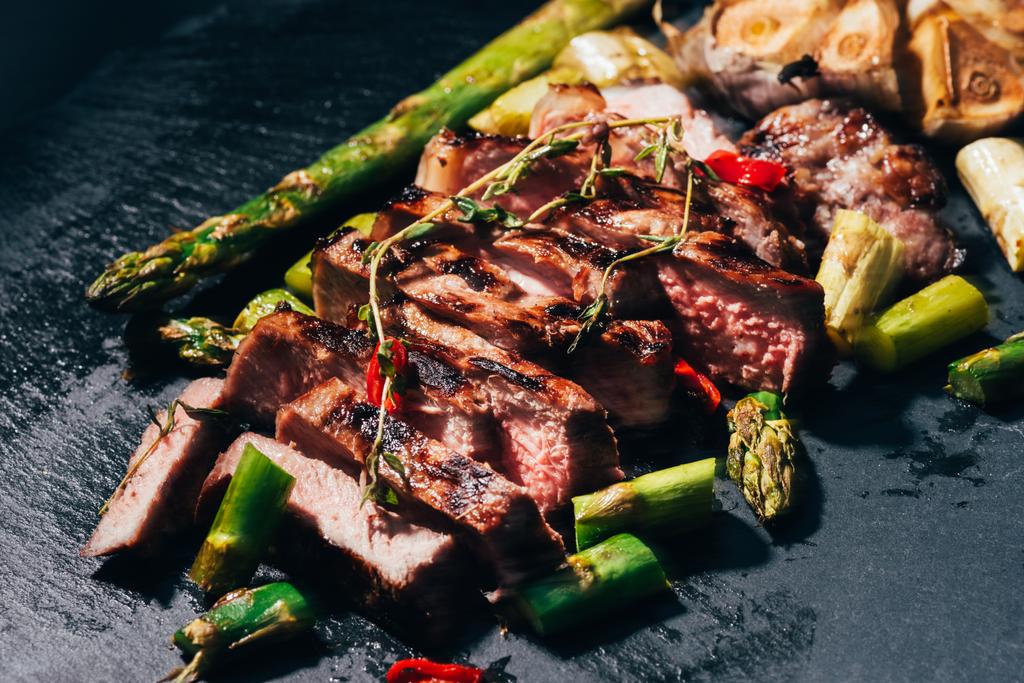 primo piano vista di gourmet affettati carne alla griglia con asparagi e spezie su nero
 - Foto, immagini