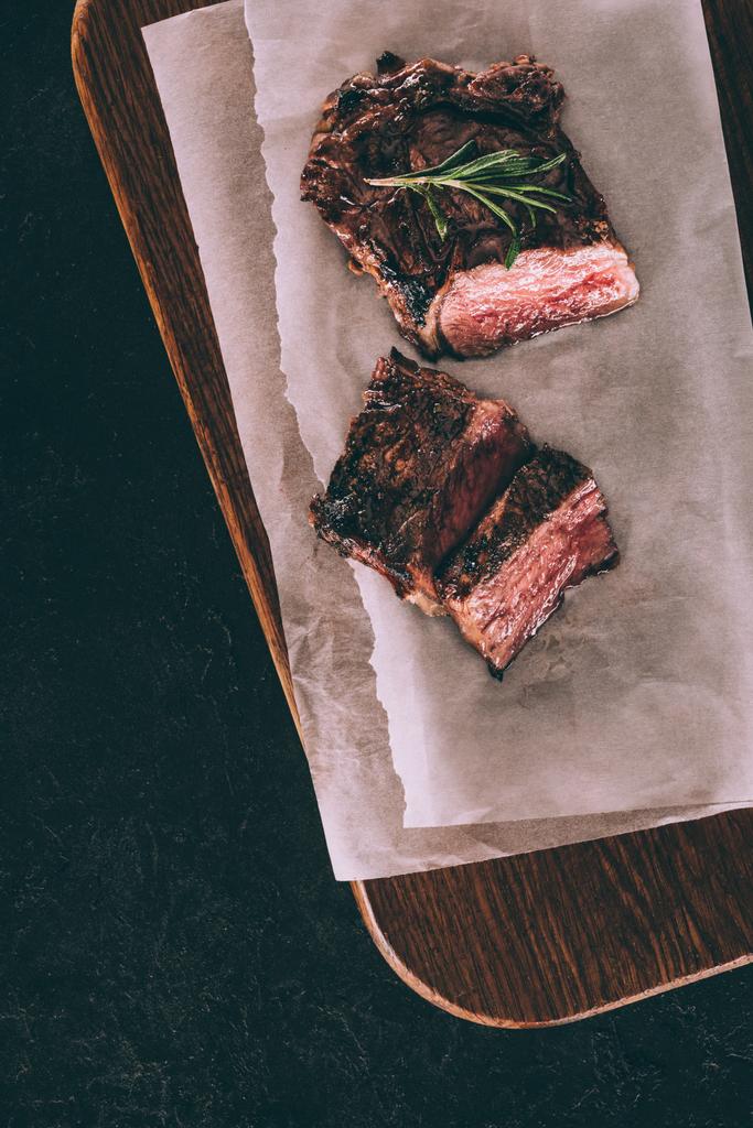 вид сверху на вкусное мясо на гриле с розмарином на выпечке и деревянную доску на черном
 - Фото, изображение