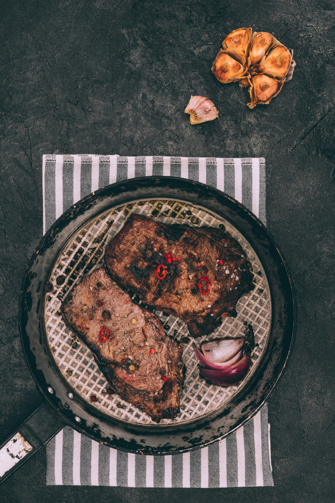 bovenaanzicht van gourmet steaks op koekenpan geroosterd en gegrilde knoflook op zwart - Foto, afbeelding