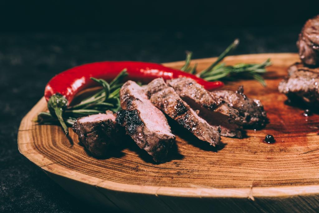 vista de cerca de la deliciosa carne a la parrilla en rodajas con romero y chile sobre tabla de madera
 - Foto, imagen