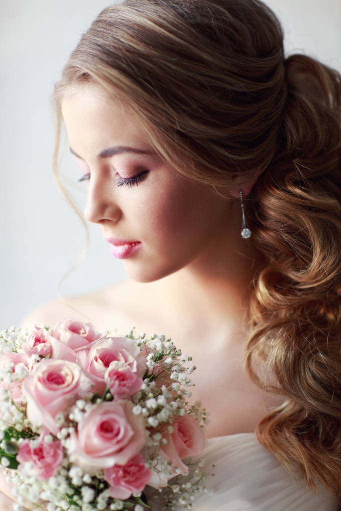 Modeporträt einer jungen schönen Frau im weißen Hochzeitskleid, die mit einem Strauß rosa Rosen posiert  - Foto, Bild