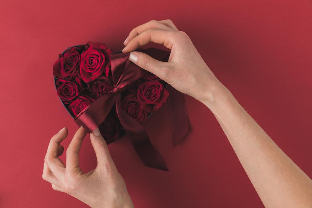 częściowy widok kobiety wiązanie wstążki na serce w kształcie pole z różami na czerwonym stole, st Walentynki koncepcji - Zdjęcie, obraz