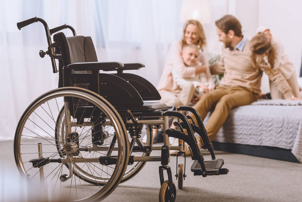 Glücklicher Vater mit Behinderung und Mutter mit Kindern im Bett mit Rollstuhl im Vordergrund - Foto, Bild