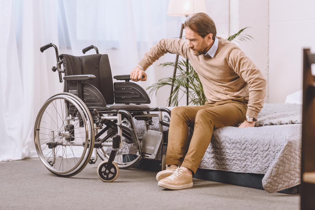 człowiek z niepełnosprawnością próbuje siedzieć na wózku inwalidzkim z łóżkiem - Zdjęcie, obraz
