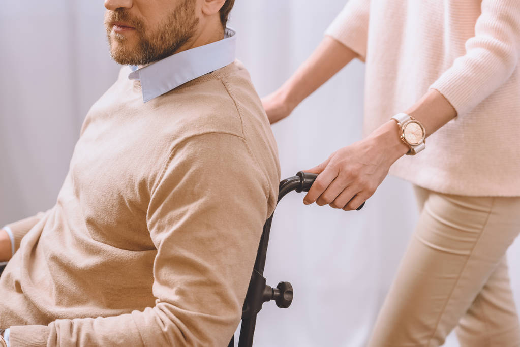 rajattu kuva vaimosta, joka kantaa miestä pyörätuolissa
 - Valokuva, kuva