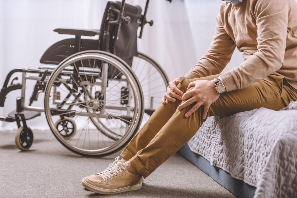 обрізане зображення людини з інвалідністю, що сидить на ліжку і торкається ніг
 - Фото, зображення