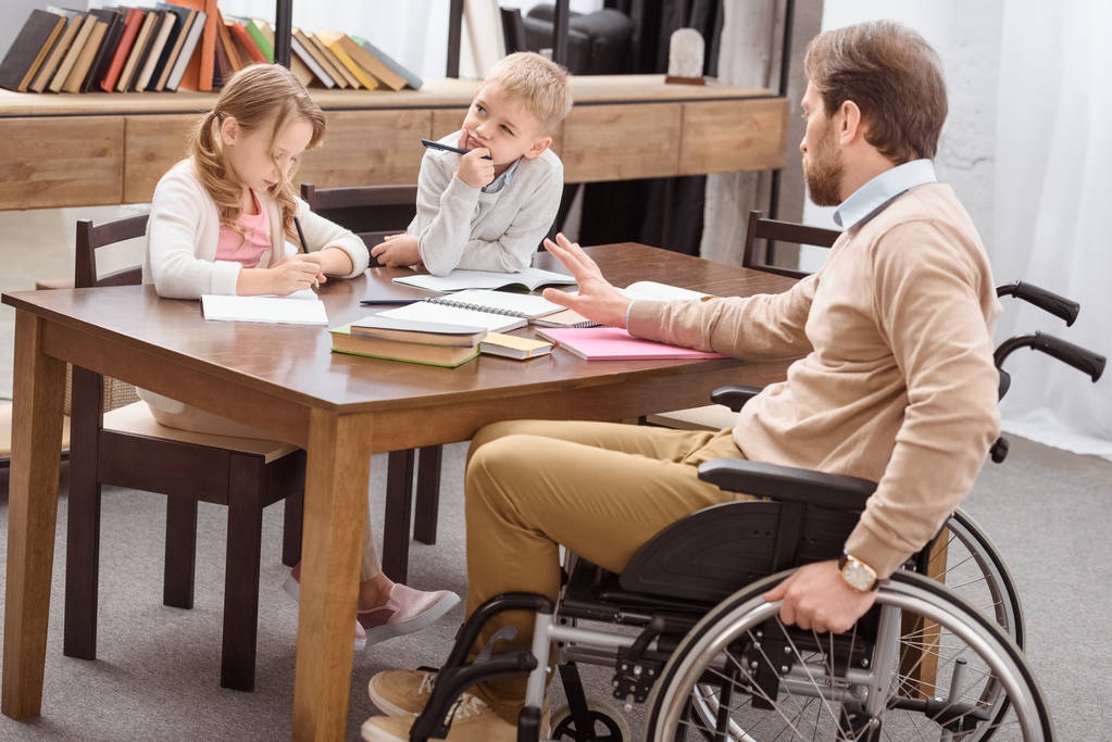 pai em cadeira de rodas ajudando filha e filho com educação em casa
 - Foto, Imagem