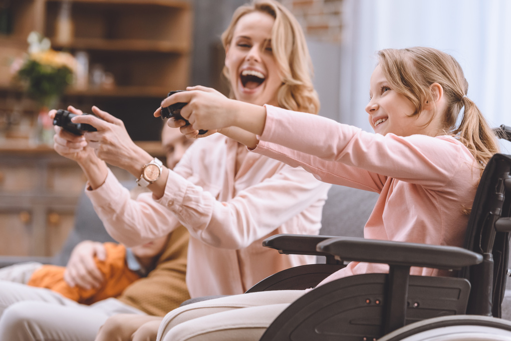 familia alegre con niño discapacitado en silla de ruedas jugando con joysticks juntos en casa
  - Foto, Imagen