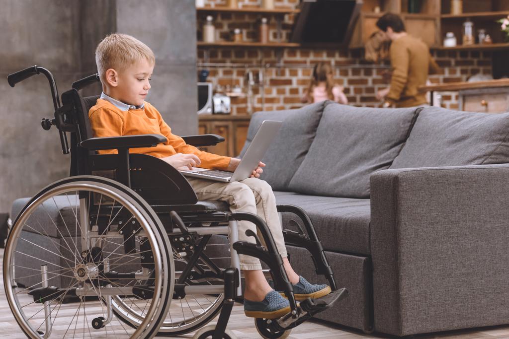 criança pequena bonito sentado em cadeira de rodas e usando laptop em casa
 - Foto, Imagem