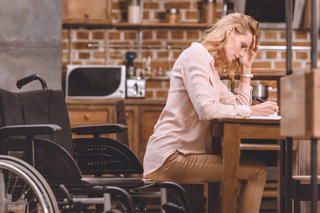 vista lateral de la mujer discapacitada en silla de ruedas tomando notas mientras trabaja en casa
 - Foto, Imagen