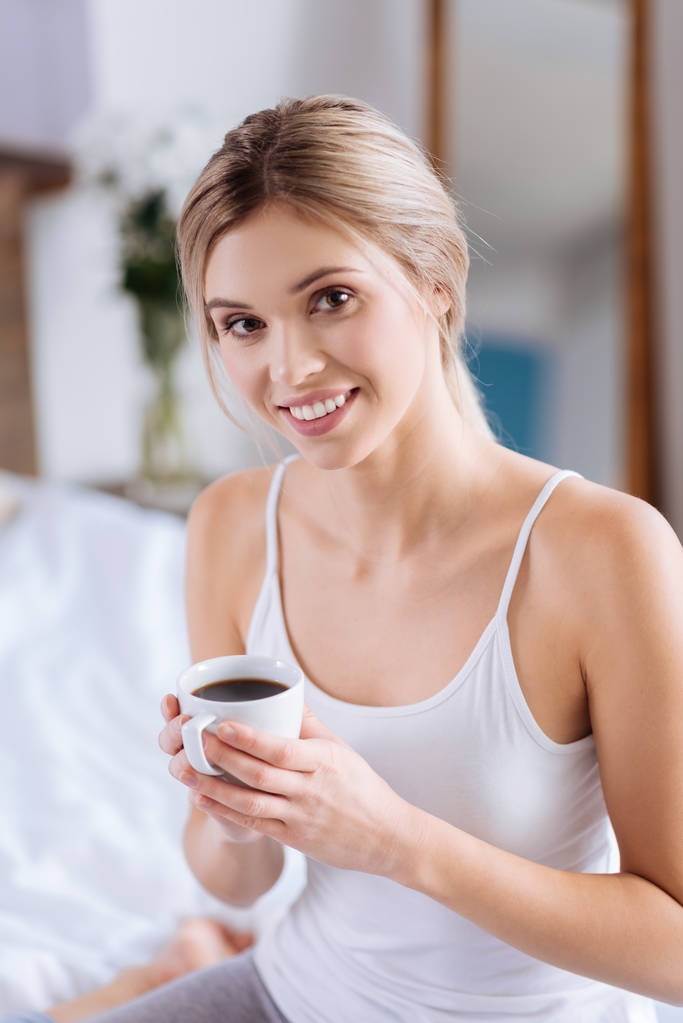 Χαρούμενη γυναίκα που ποζάρει με ένα φλιτζάνι καφέ στο υπνοδωμάτιο - Φωτογραφία, εικόνα