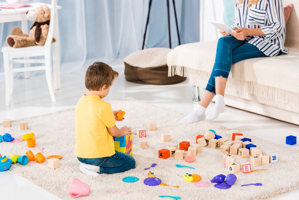 recortado tiro de mujer usando tableta mientras pequeño hijo jugando con juguetes en casa
 - Foto, Imagen