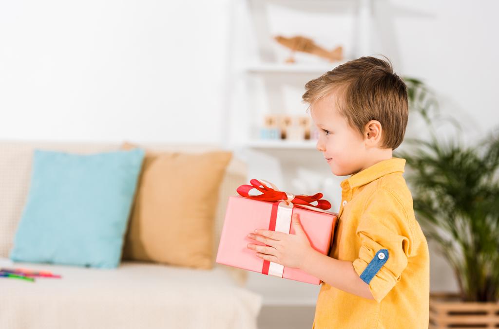 vista lateral del niño pequeño sosteniendo regalo envuelto en las manos
 - Foto, imagen