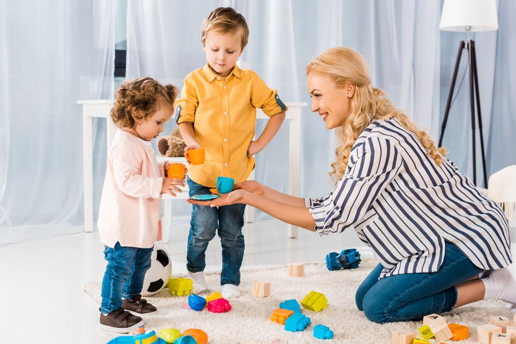 Szczęśliwa matka bawi się z synem i córką z plastikowych kubeczków - Zdjęcie, obraz