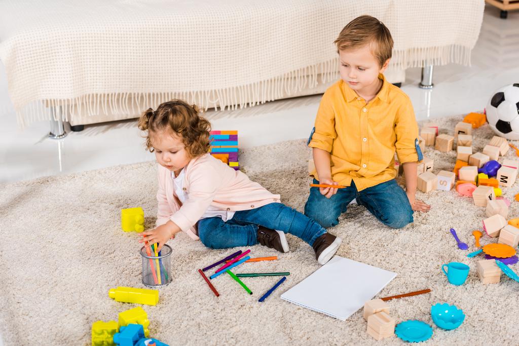 adorables frères et sœurs jouant sur un sol avec des crayons de couleur
 - Photo, image