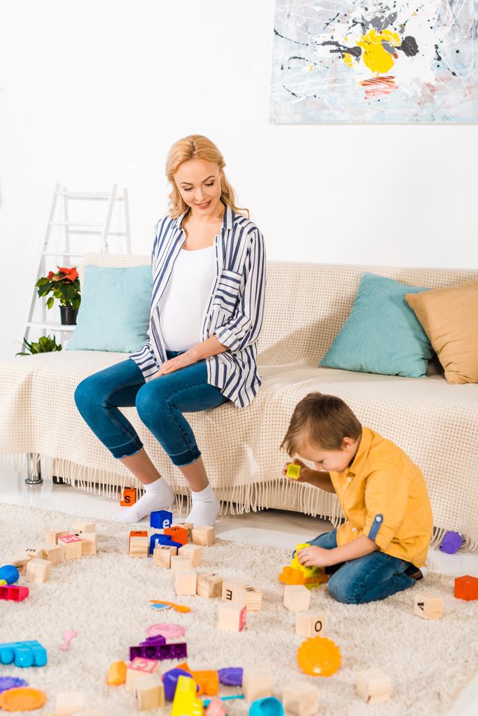 happy pregnant mother looking how son playing plastic blocks - Photo, Image