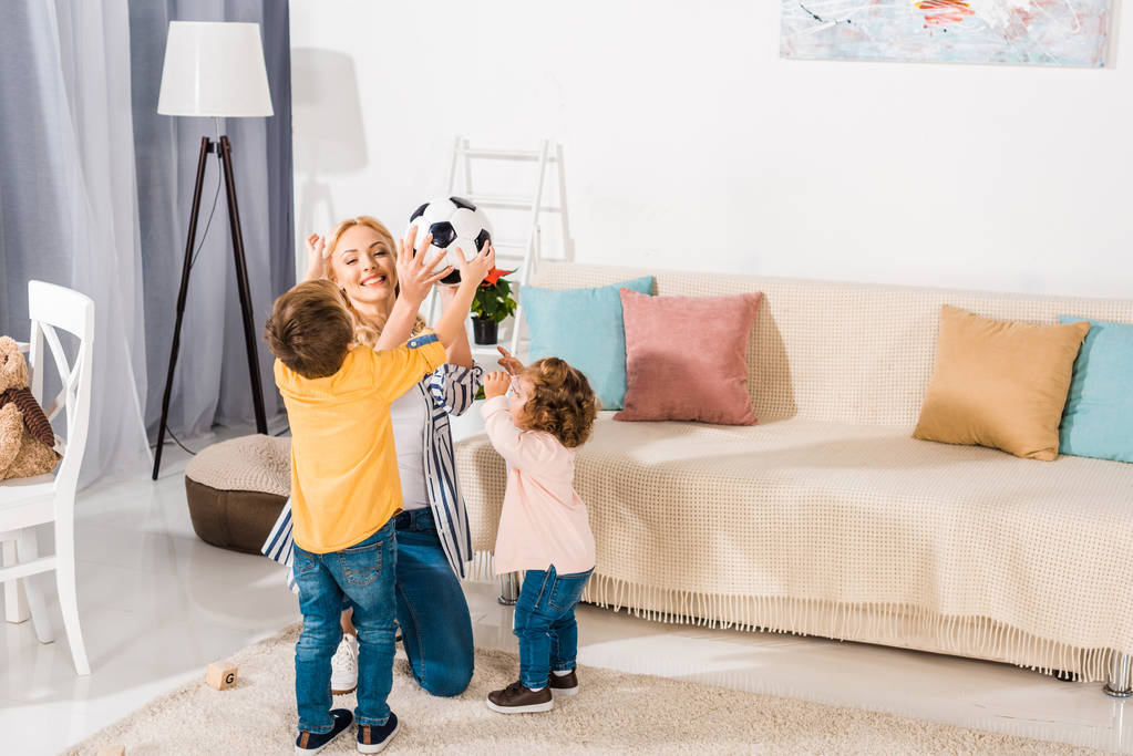 счастливая мать и очаровательные маленькие дети держат футбольный мяч дома
 - Фото, изображение