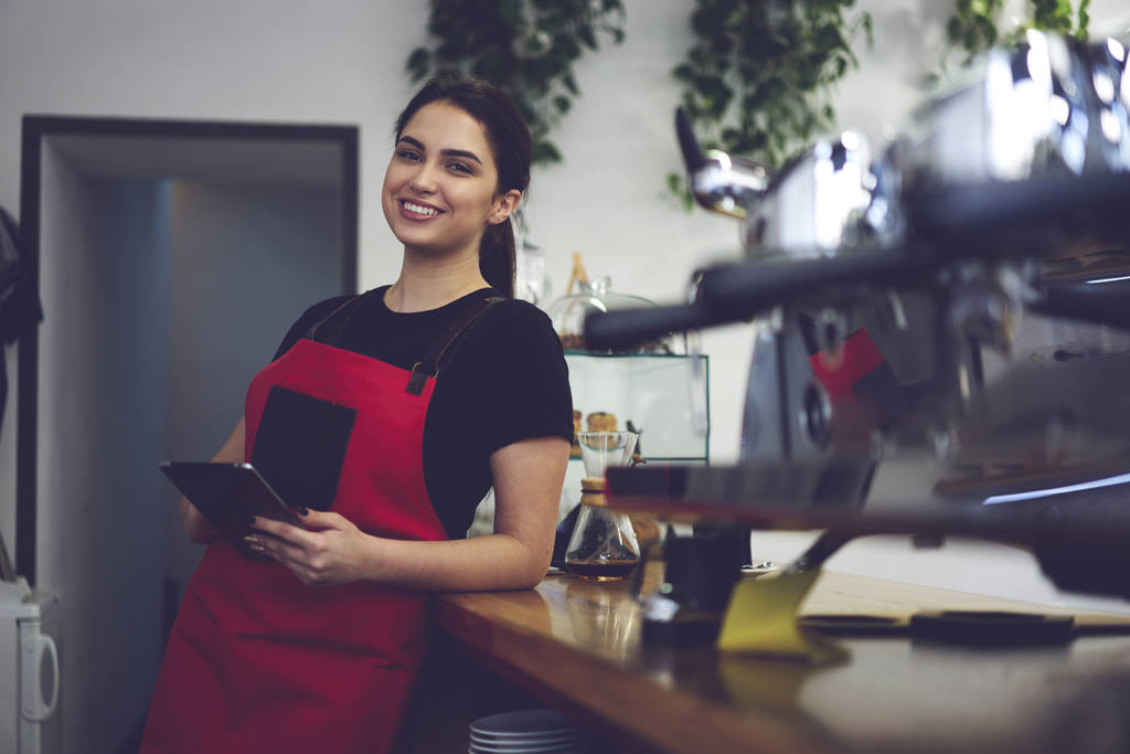 Portrait of female barista smiling to the camera holding cup of coffee - Photo, Image