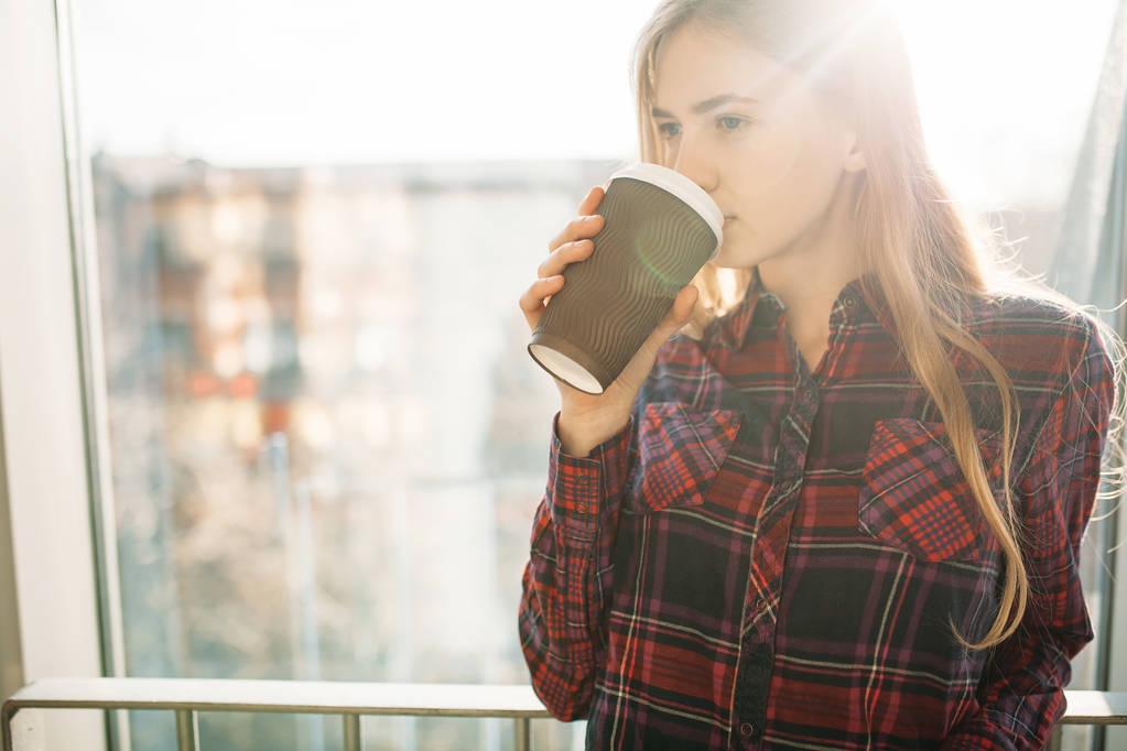 fiatal gyönyörű lány kávét inni, egy nő egy irodában, épületben, a fényes nap - Fotó, kép